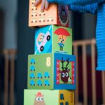 Home A child playing indoors, stacking colorful wooden toy blocks with joyful illustrations.